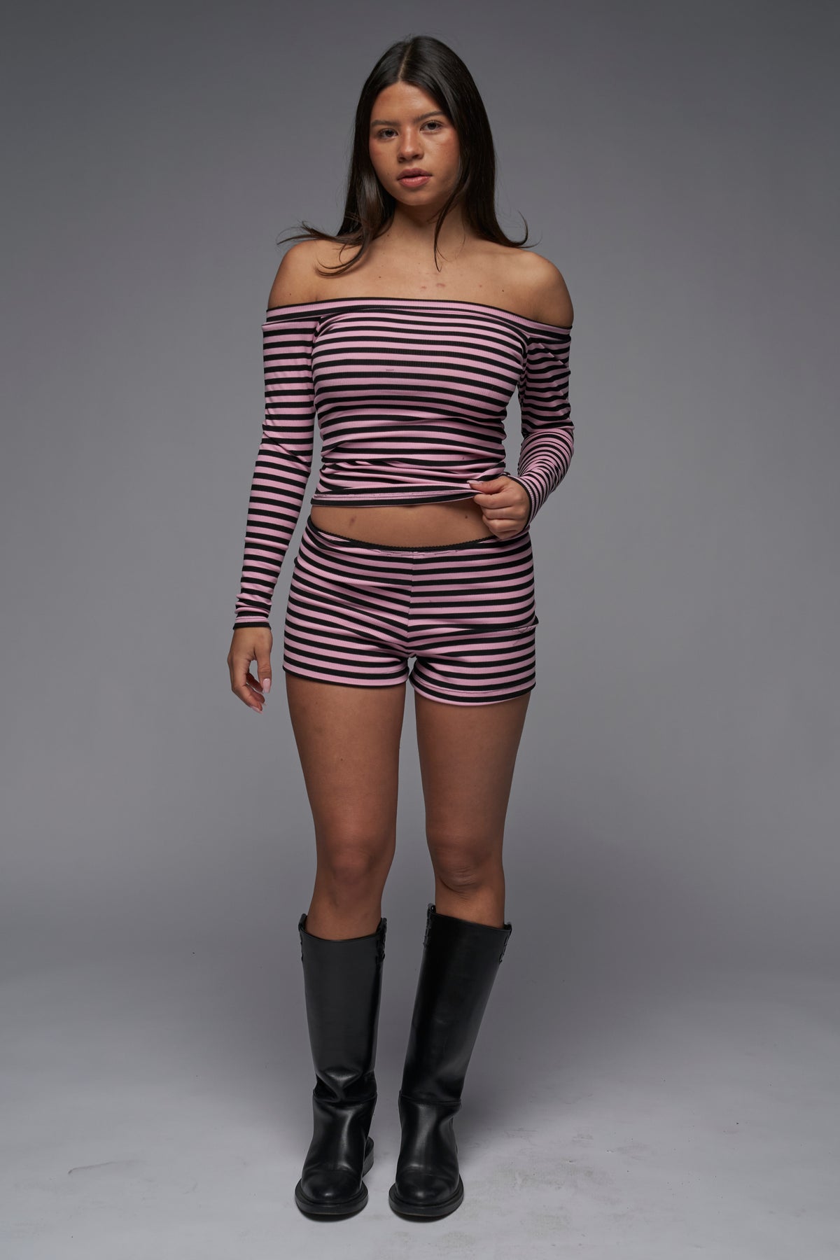 This image features a stylish ensemble of the "Riley Shorts" in a pink and black striped pattern. The shorts are paired with a matching off-the-shoulder long-sleeve top, showcasing a comfortable and trendy look.