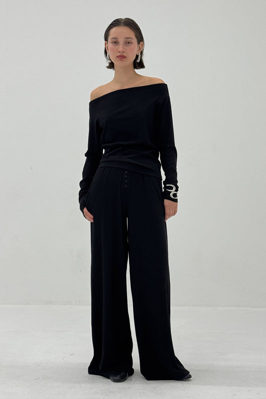 Person wearing a black off-shoulder top and wide-leg pants on a white background