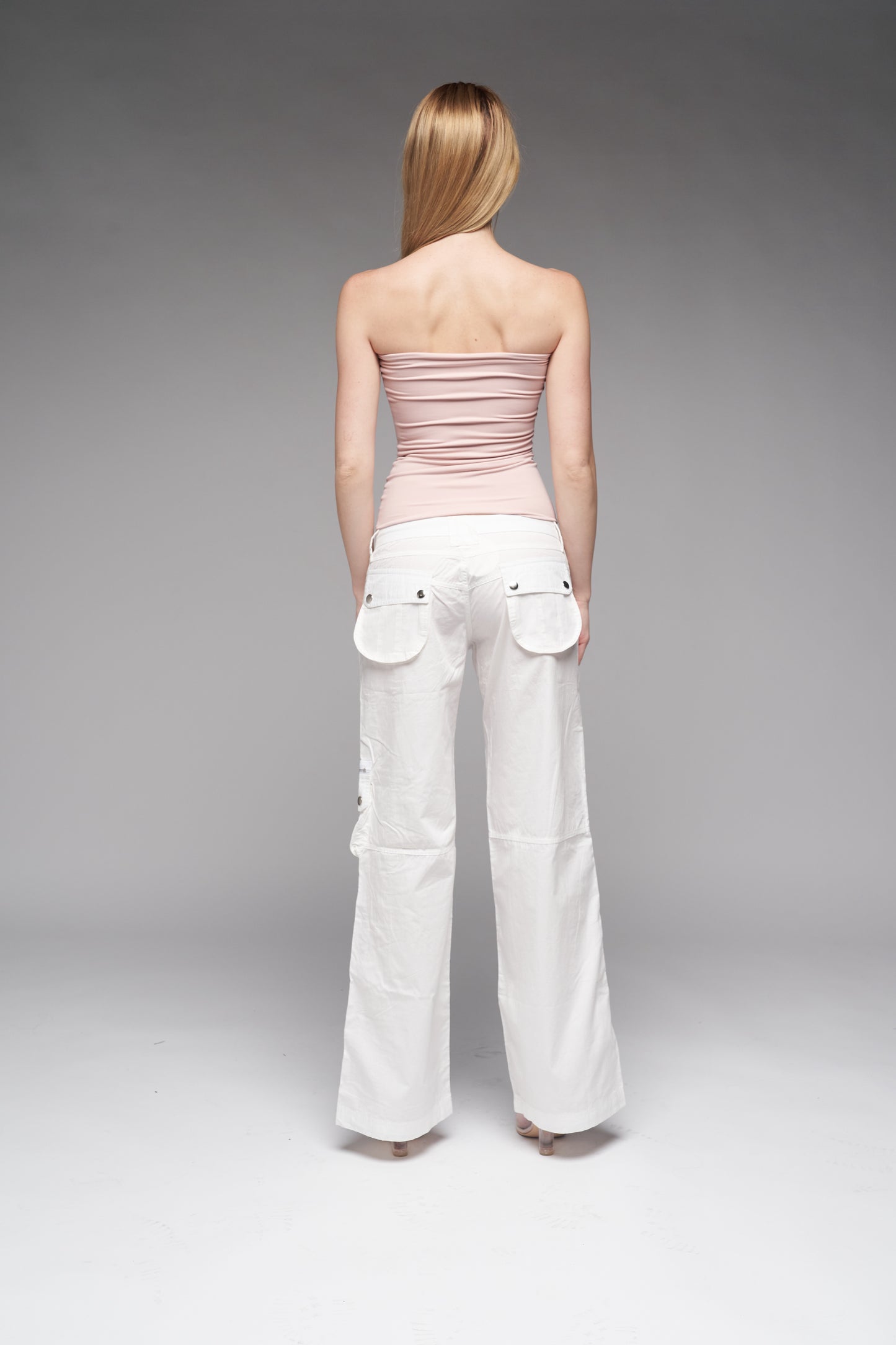 Woman wearing a strapless pink top and white pants on a gray background