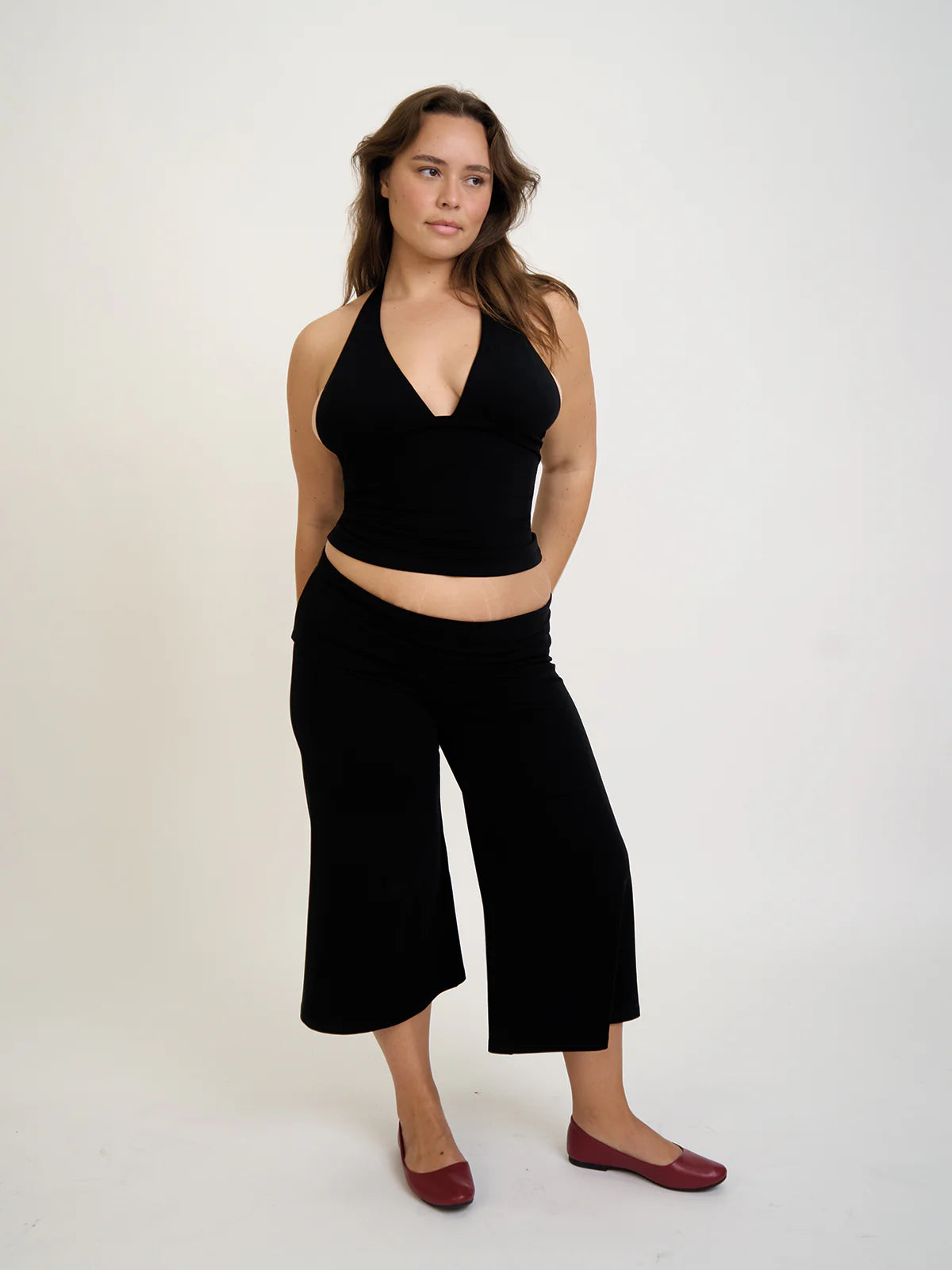 Woman wearing a black halter top and wide-leg gaucho pants on a white background