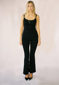 Woman wearing a black tank top and black flared pants on a plain background