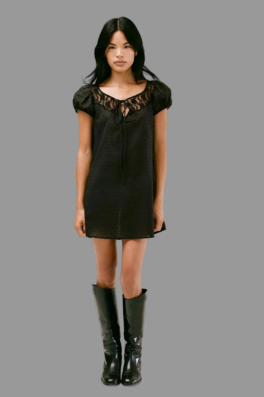 Woman wearing a short black dress with lace details and black rain boots on a white background