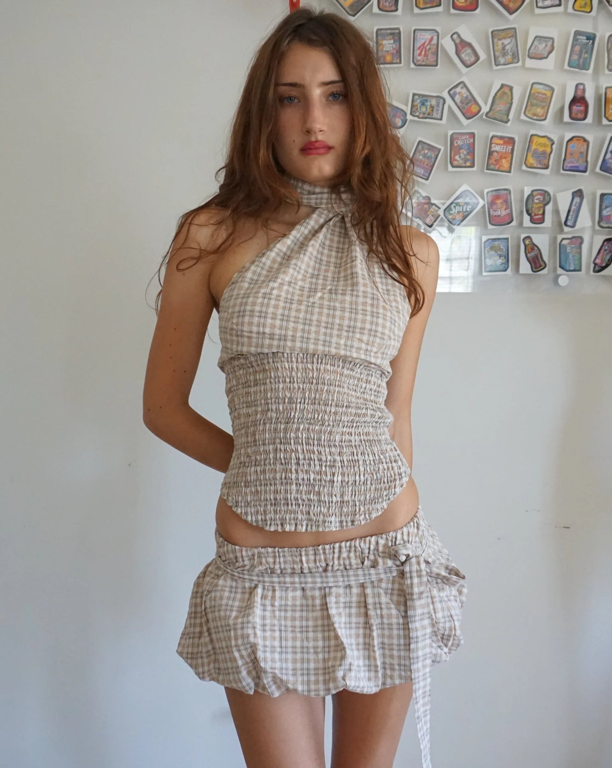 Woman wearing a checkered set standing against a wall with decorative items.