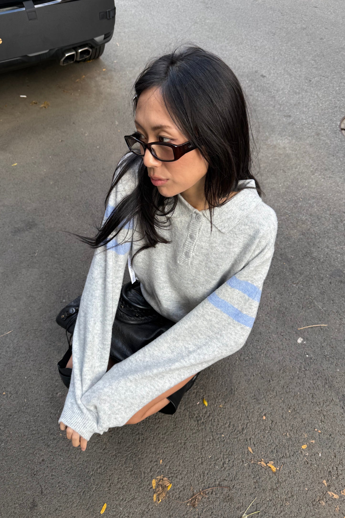 Person sitting on a concrete surface wearing a gray sweater with blue stripes.