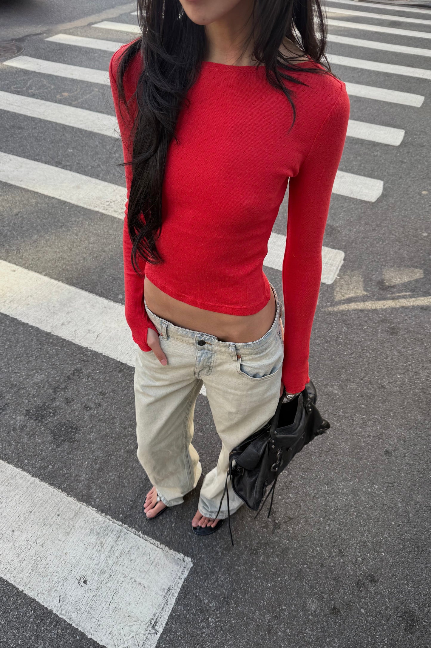 Person wearing a red long-sleeve top and light-colored pants on a crosswalk.