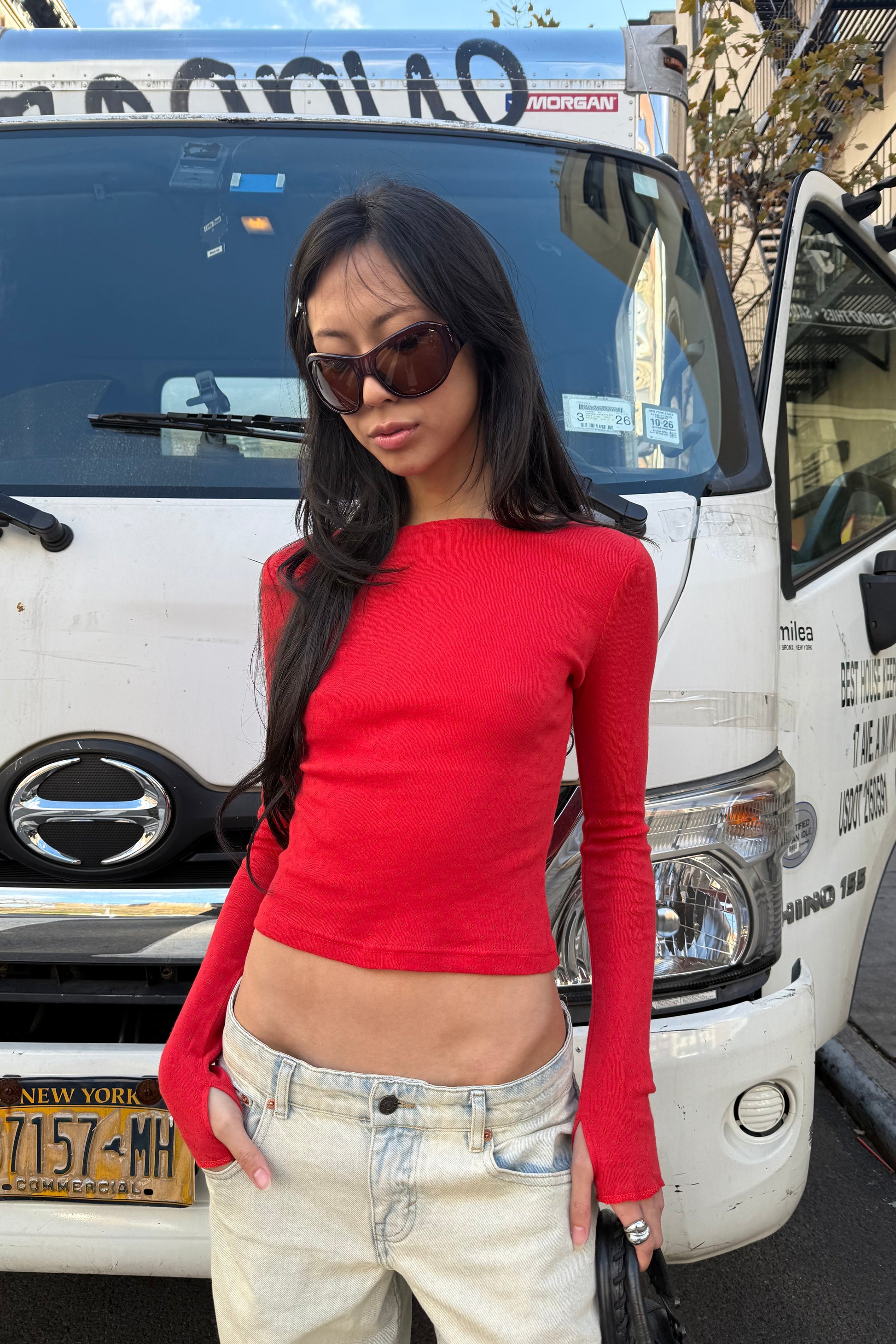 Woman in red top and beige shorts standing next to a white truck with visible license plate.