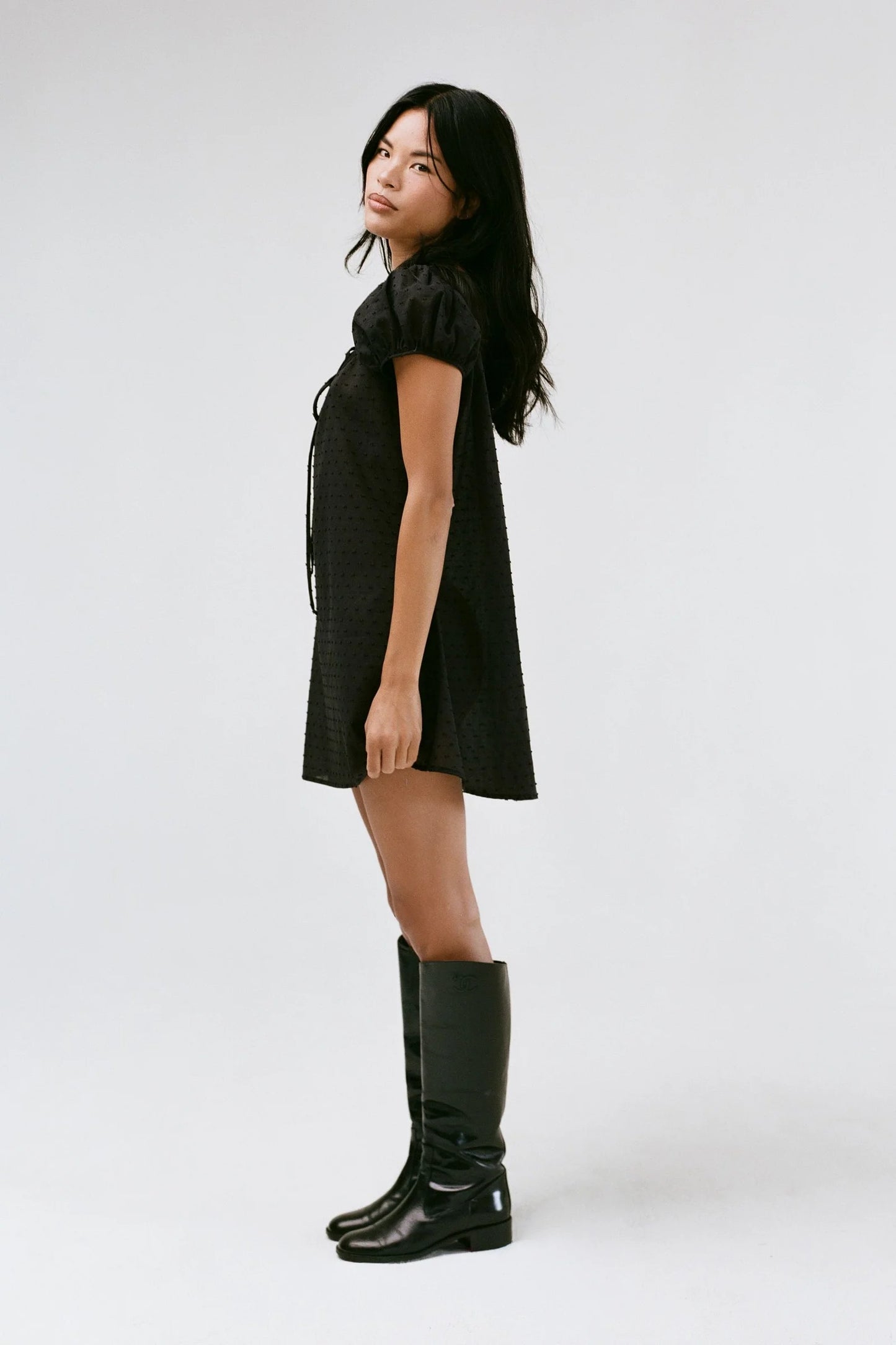 Woman wearing a black dress and black knee-high boots on a white background