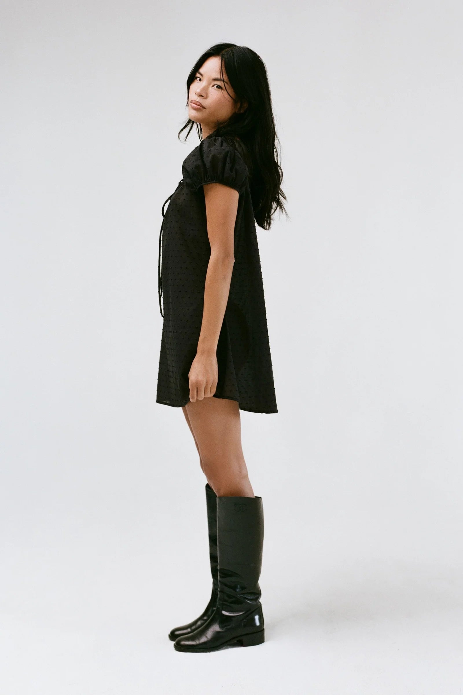 Woman wearing a black dress and black knee-high boots on a white background