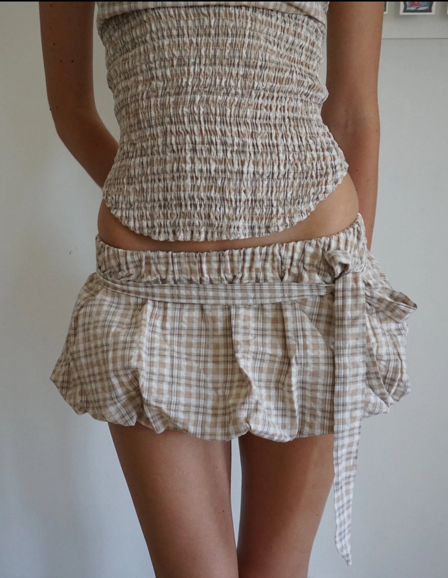 Person wearing a checkered outfit with a top and skirt against a plain background