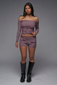 This image features a stylish ensemble of the "Riley Shorts" in a pink and black striped pattern. The shorts are paired with a matching off-the-shoulder long-sleeve top, showcasing a comfortable and trendy look.