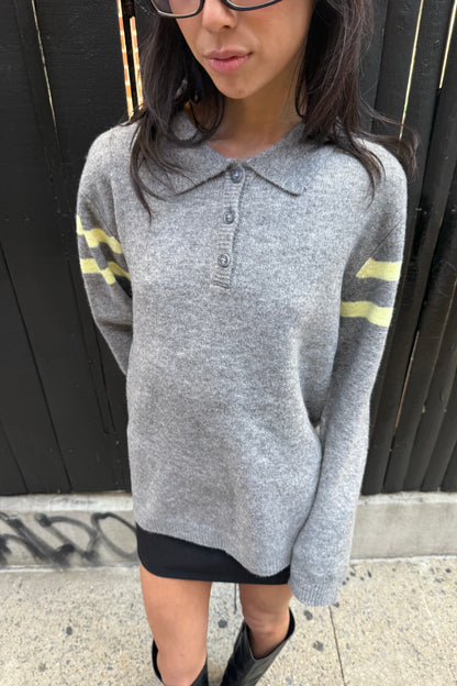 Person wearing a gray sweater with yellow accents on a sidewalk