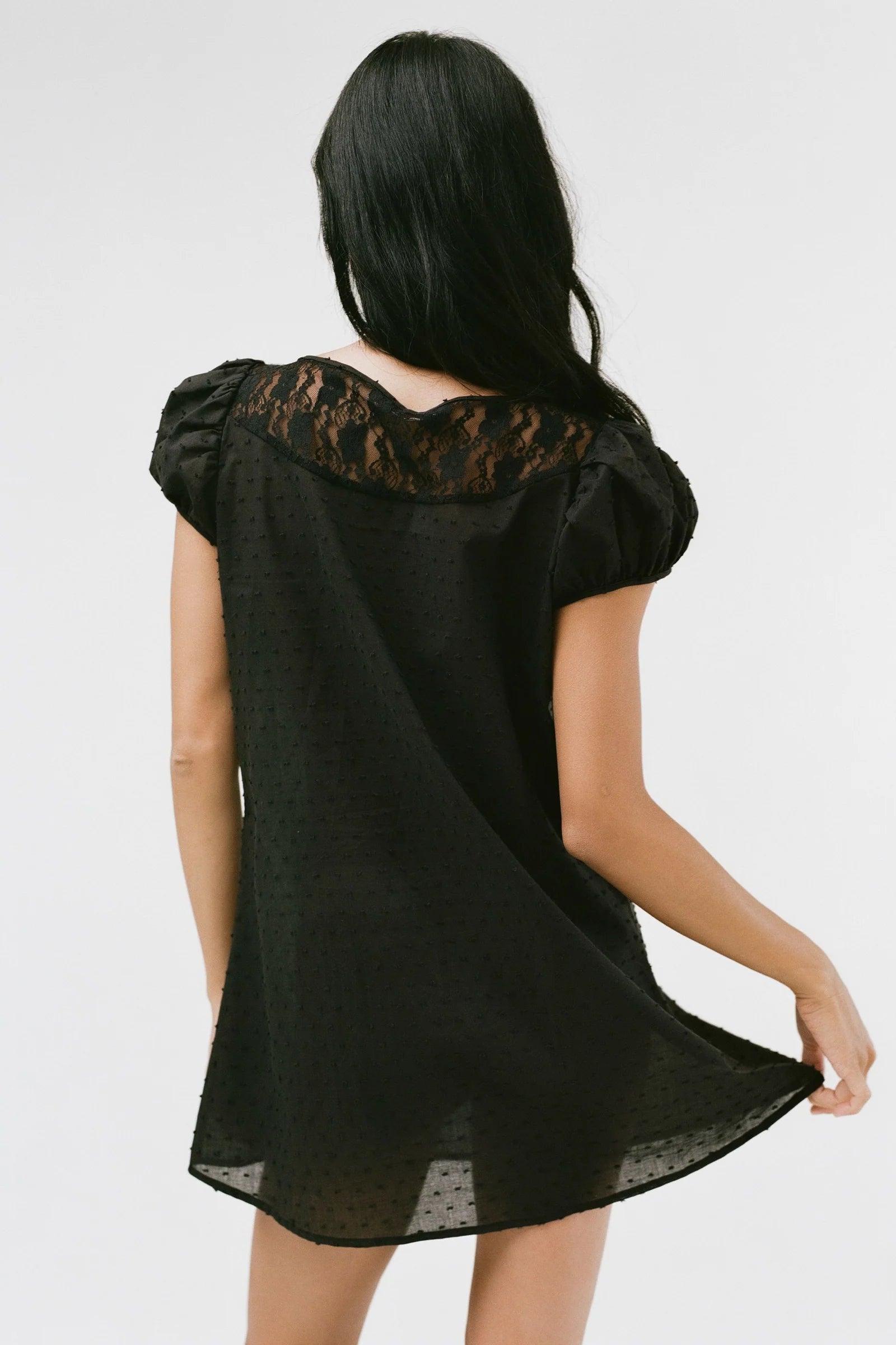 Black lace-trimmed dress worn by a person on a white background