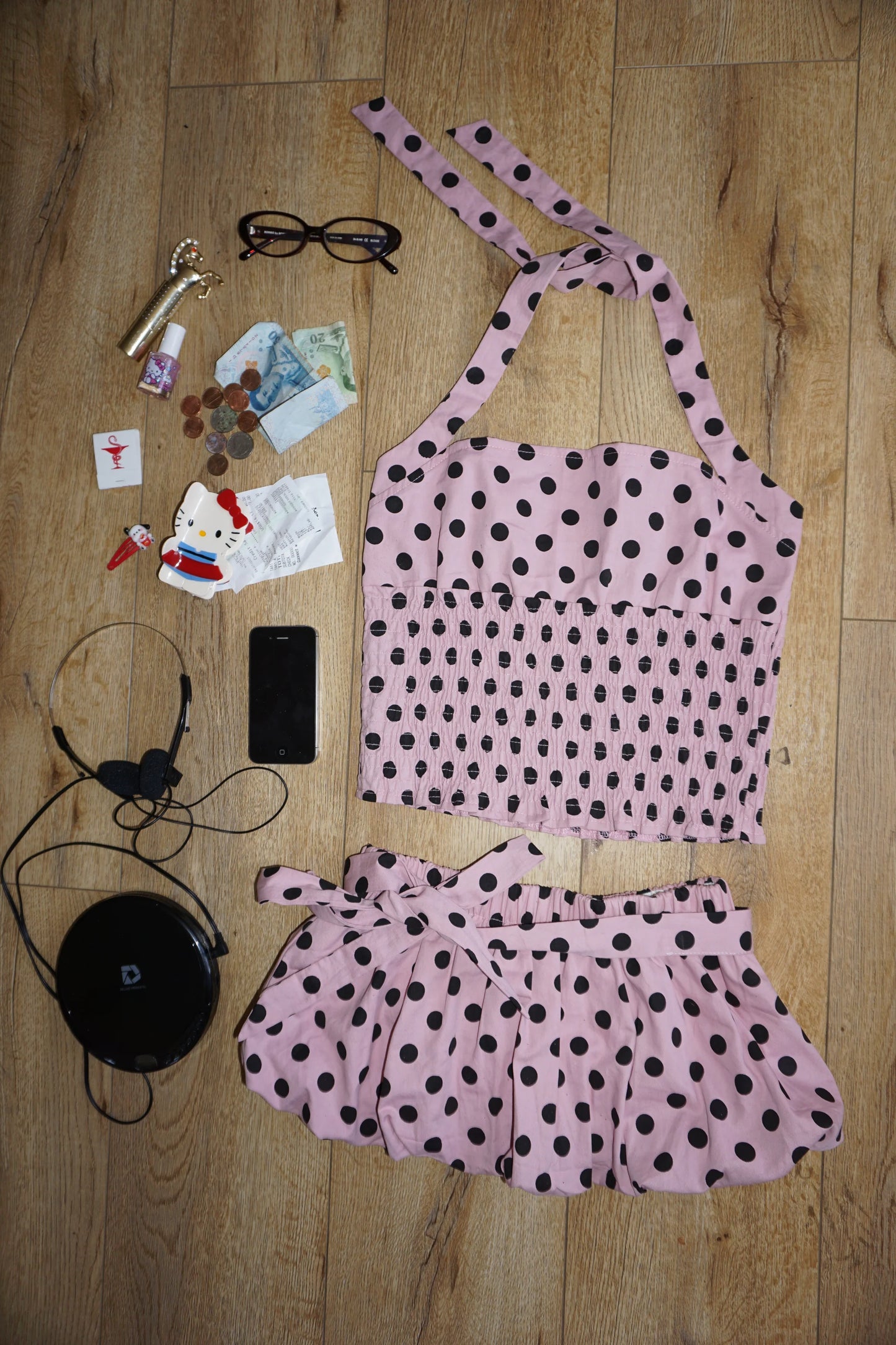 Pink polka dot top and skirt set on a wooden floor with various items.