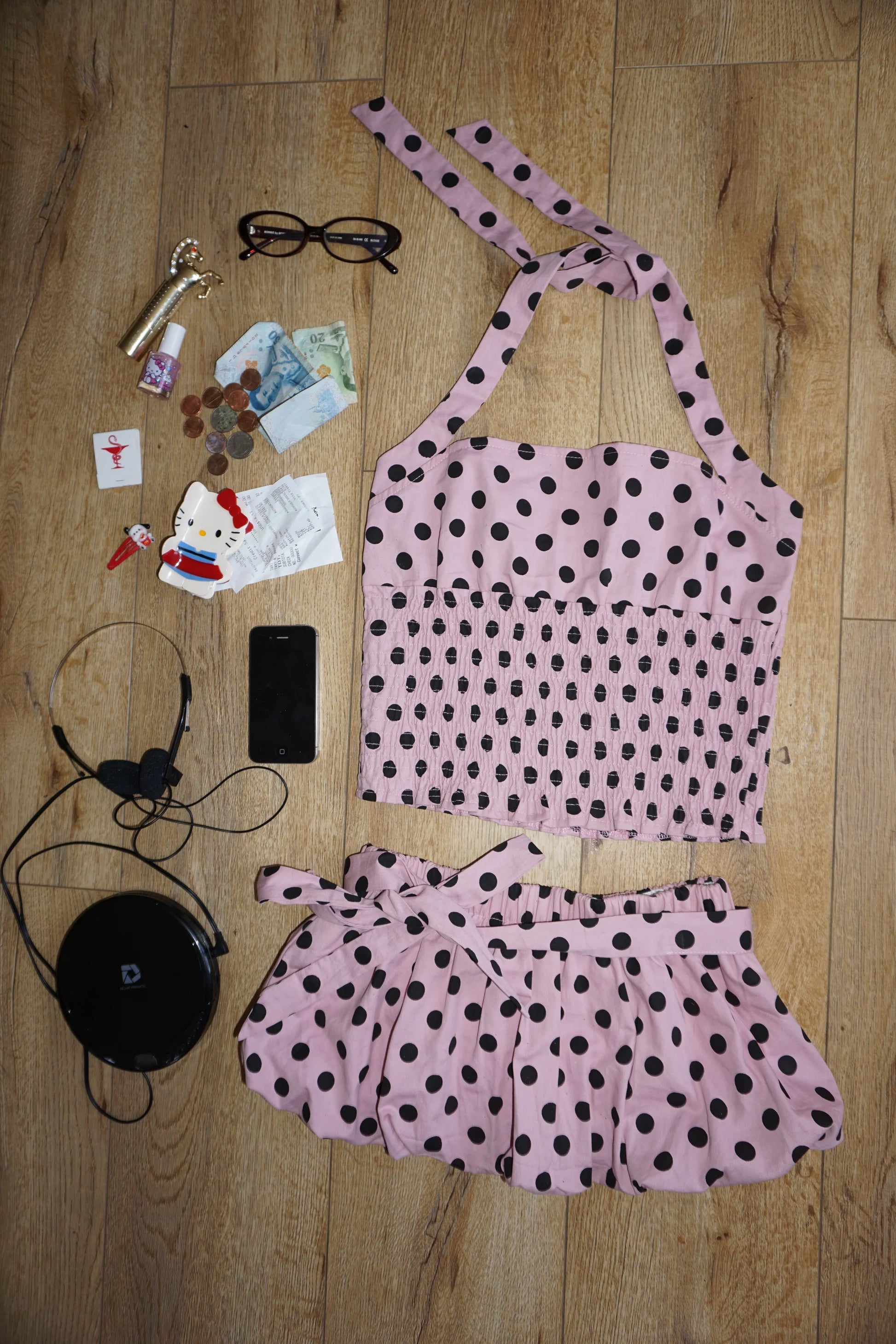 Pink polka dot top and skirt set on a wooden floor with various items.