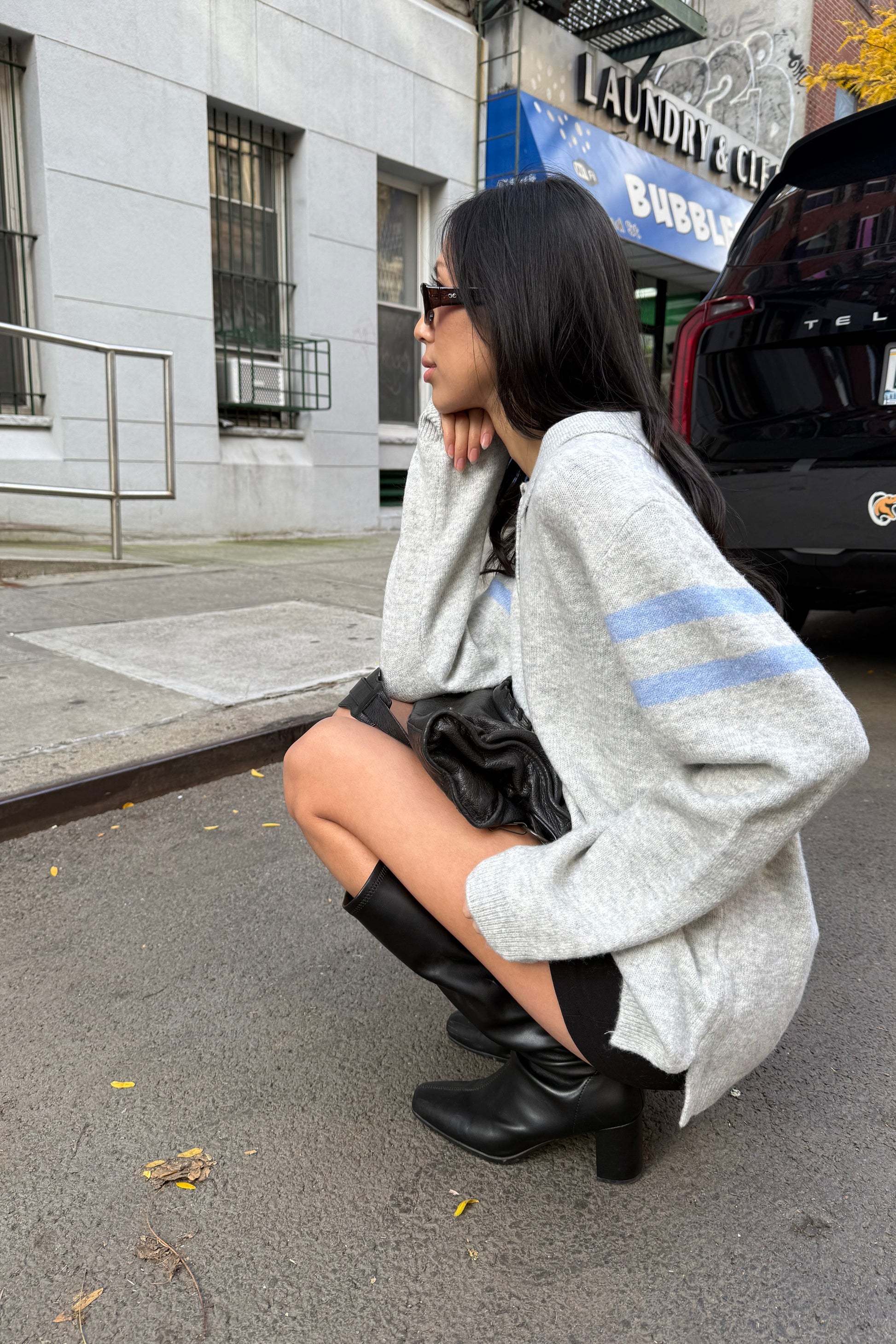 Person sitting on a road with a gray sweater and black shoes