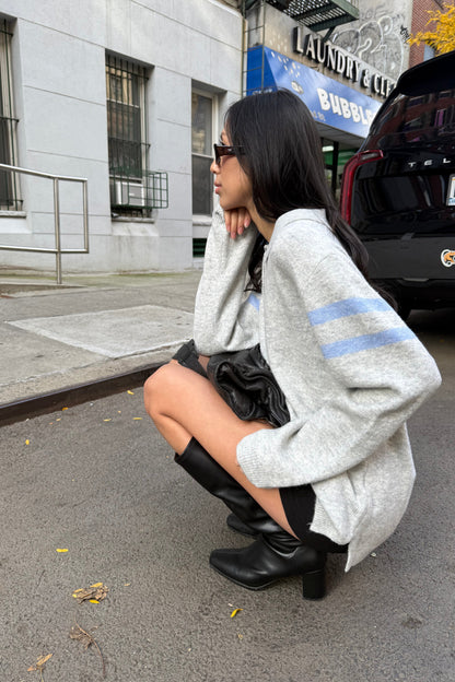 Person sitting on a road with a gray sweater and black shoes