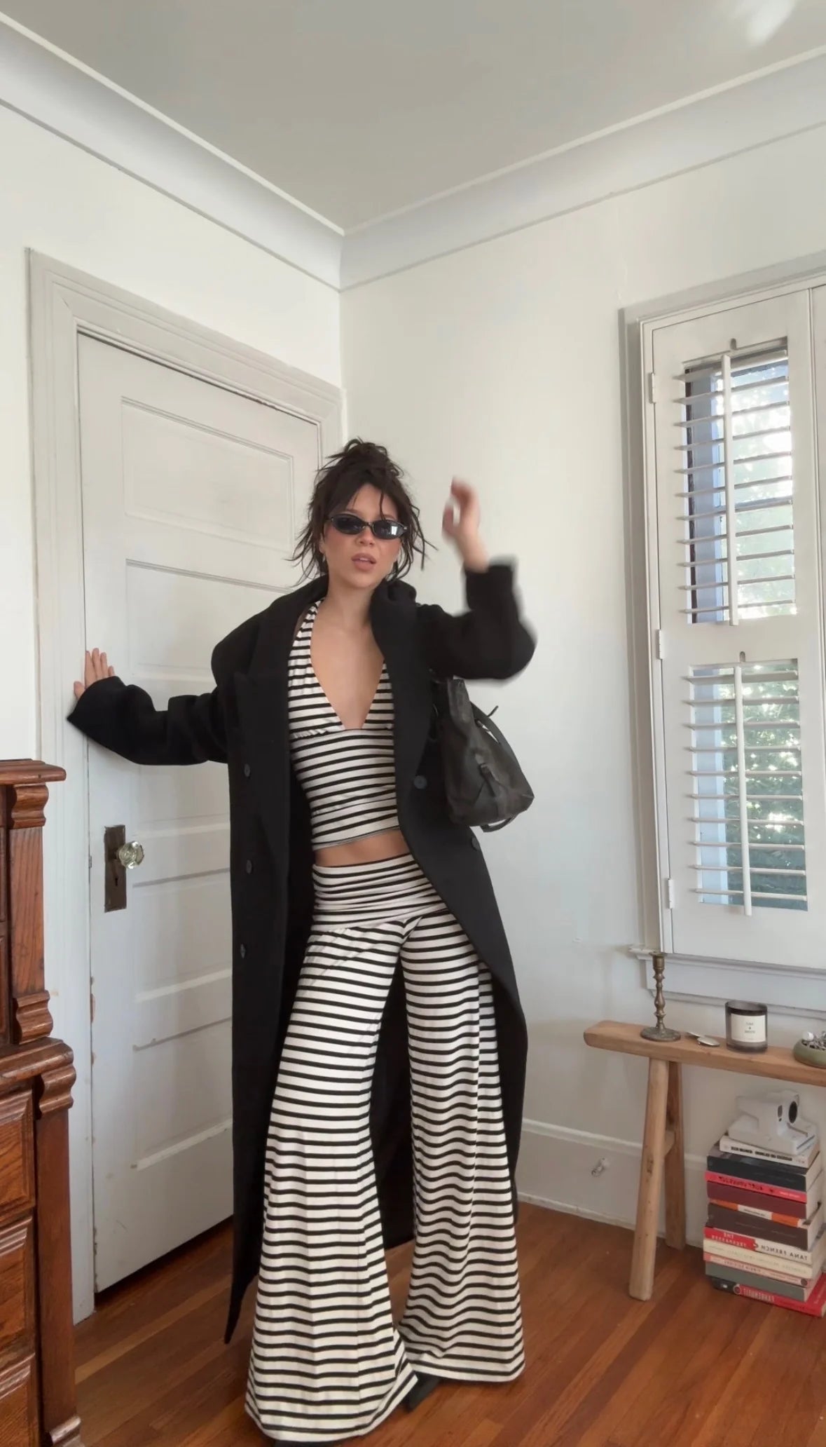 Person wearing a black coat and striped outfit in a room with a white door and window.
