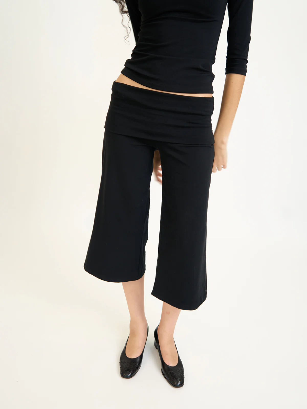 Person wearing black cropped capri pants and a black top on a white background