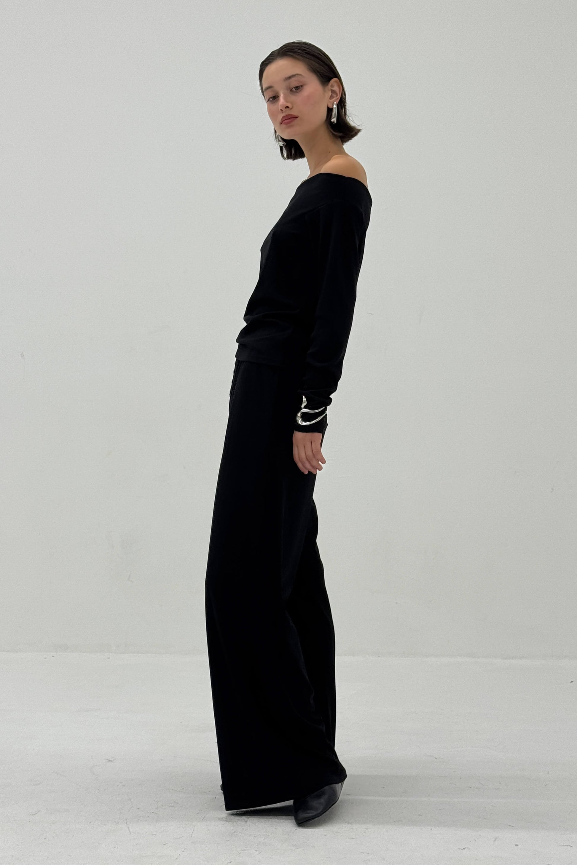 Woman wearing a black off the shoulder long-sleeve against a white background