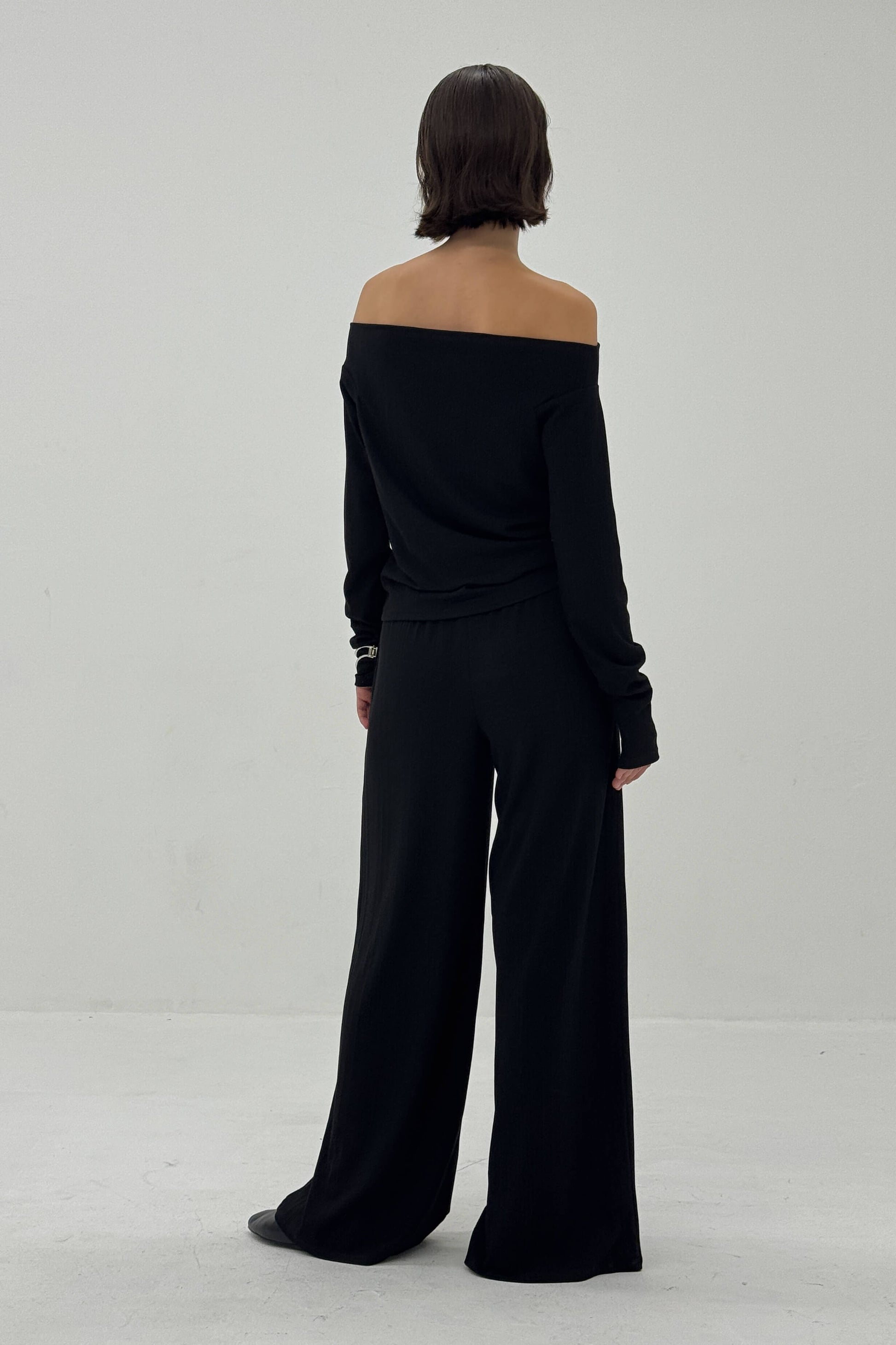 Person wearing a black off-shoulder top and wide-leg pants on a white background