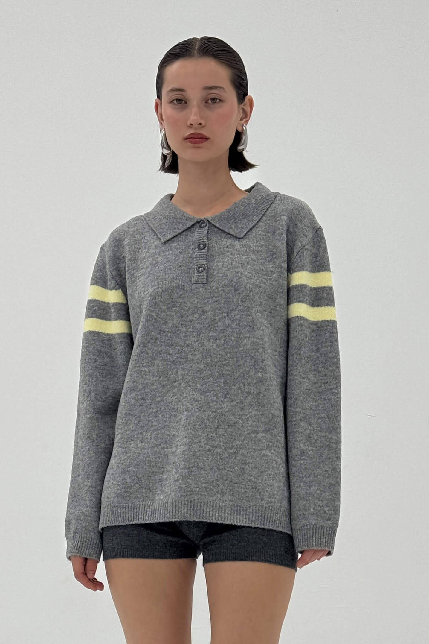 Person wearing a gray sweater with yellow stripes on a plain background