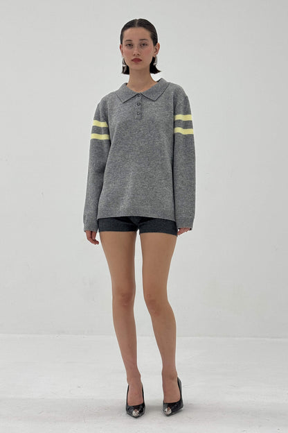 Woman wearing a gray sweater with yellow stripes and black shorts on a white background