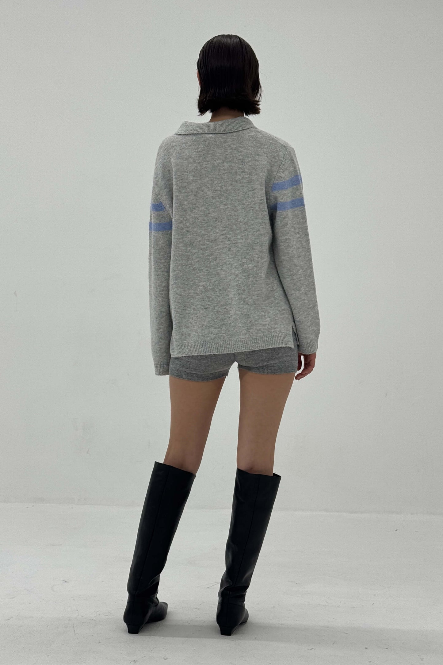 Person wearing a gray sweater with blue stripes and shorts, standing against a plain background