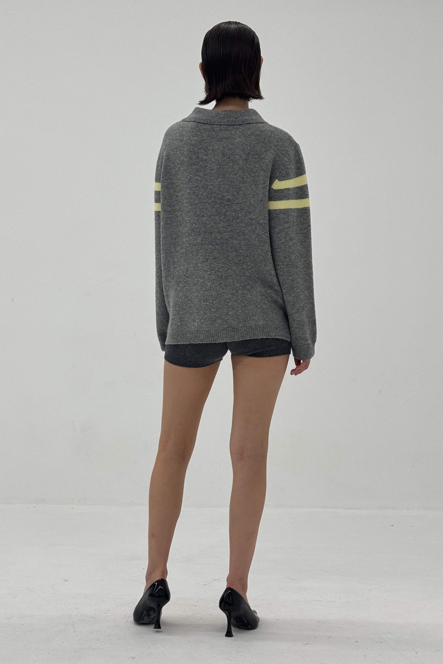Person wearing a gray sweater with yellow stripes on sleeves against a white background