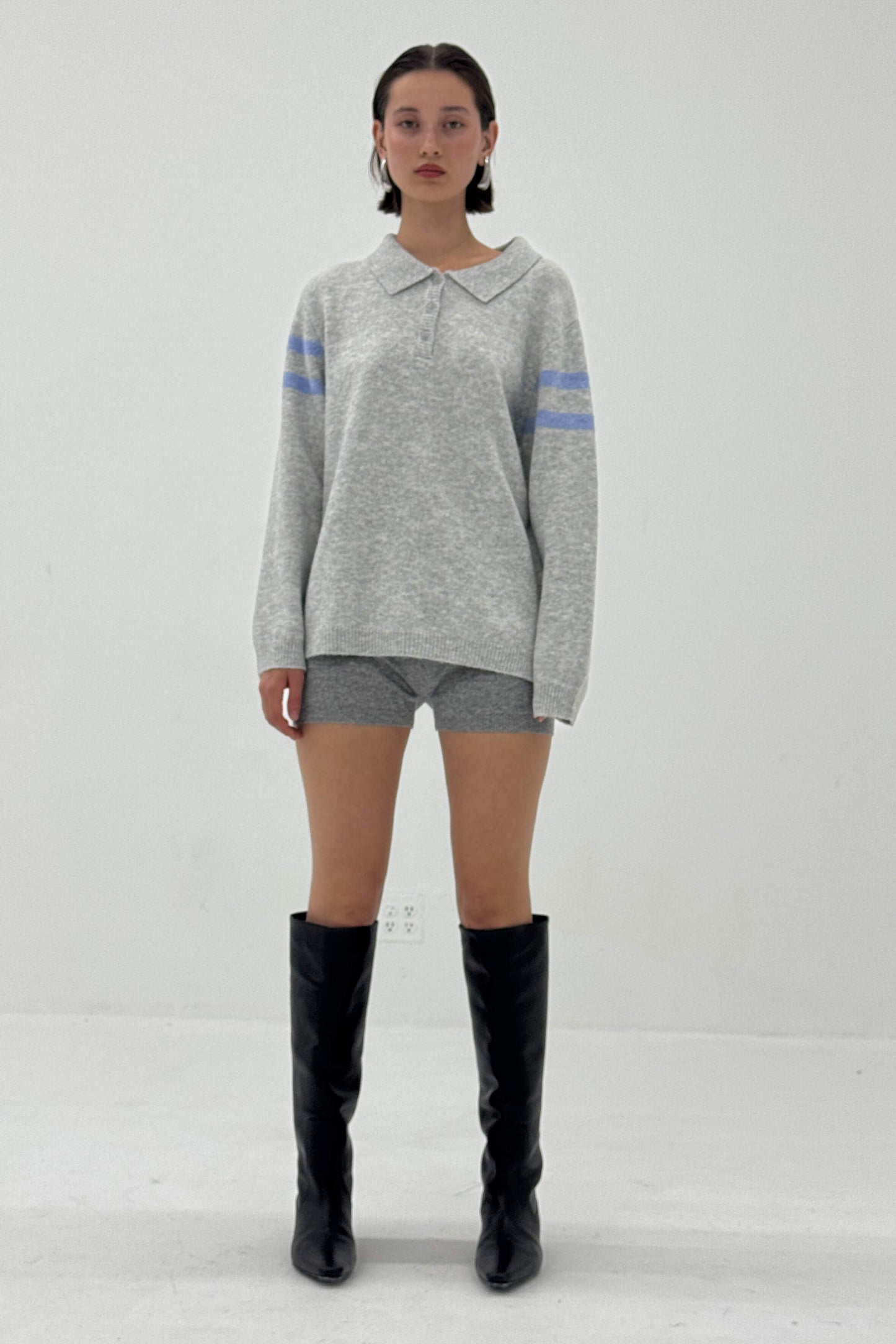 Person wearing a gray sweater with blue stripes, gray shorts, and black knee-high boots on a white background
