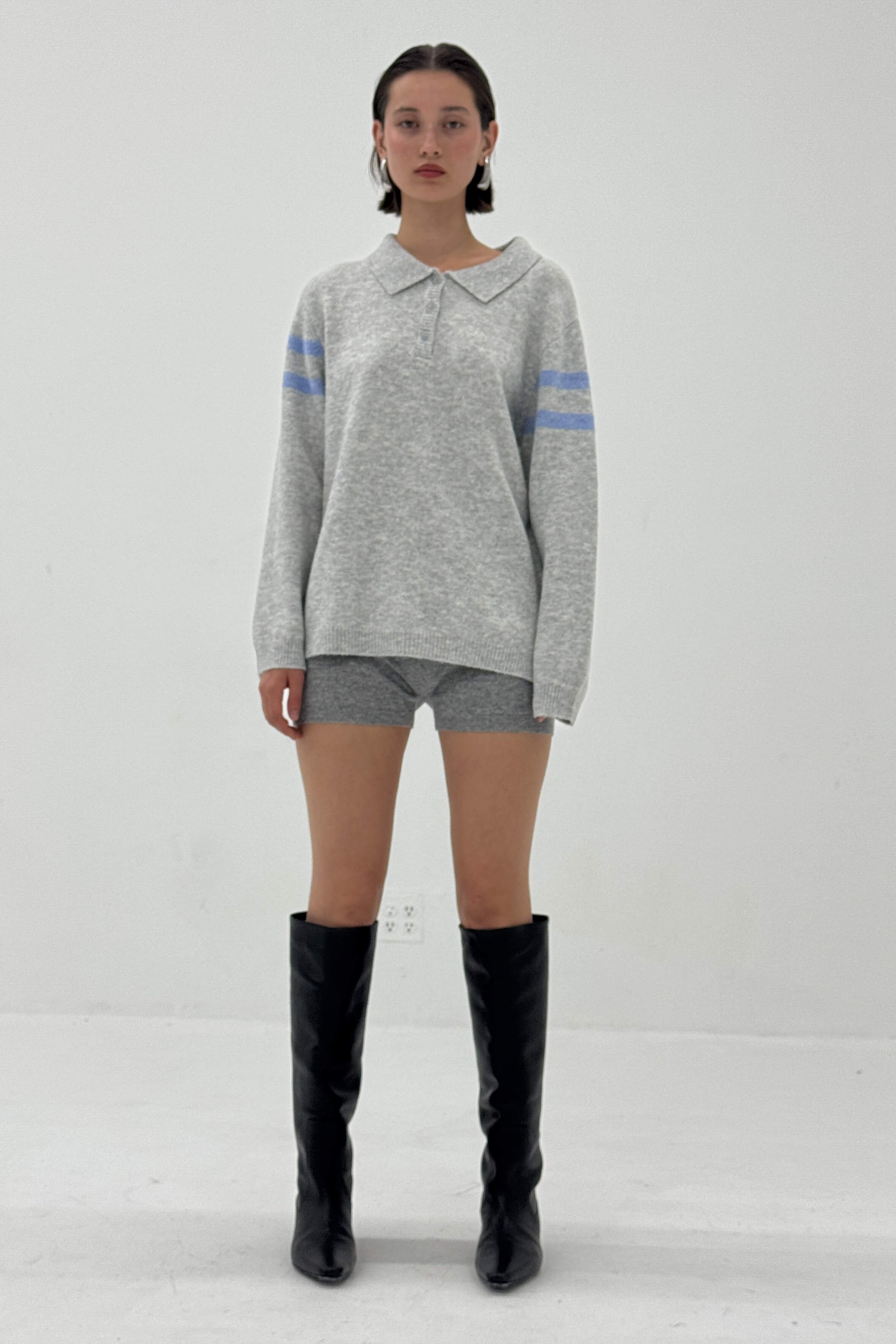 Person wearing a gray sweater with blue stripes, gray shorts, and black knee-high boots on a white background