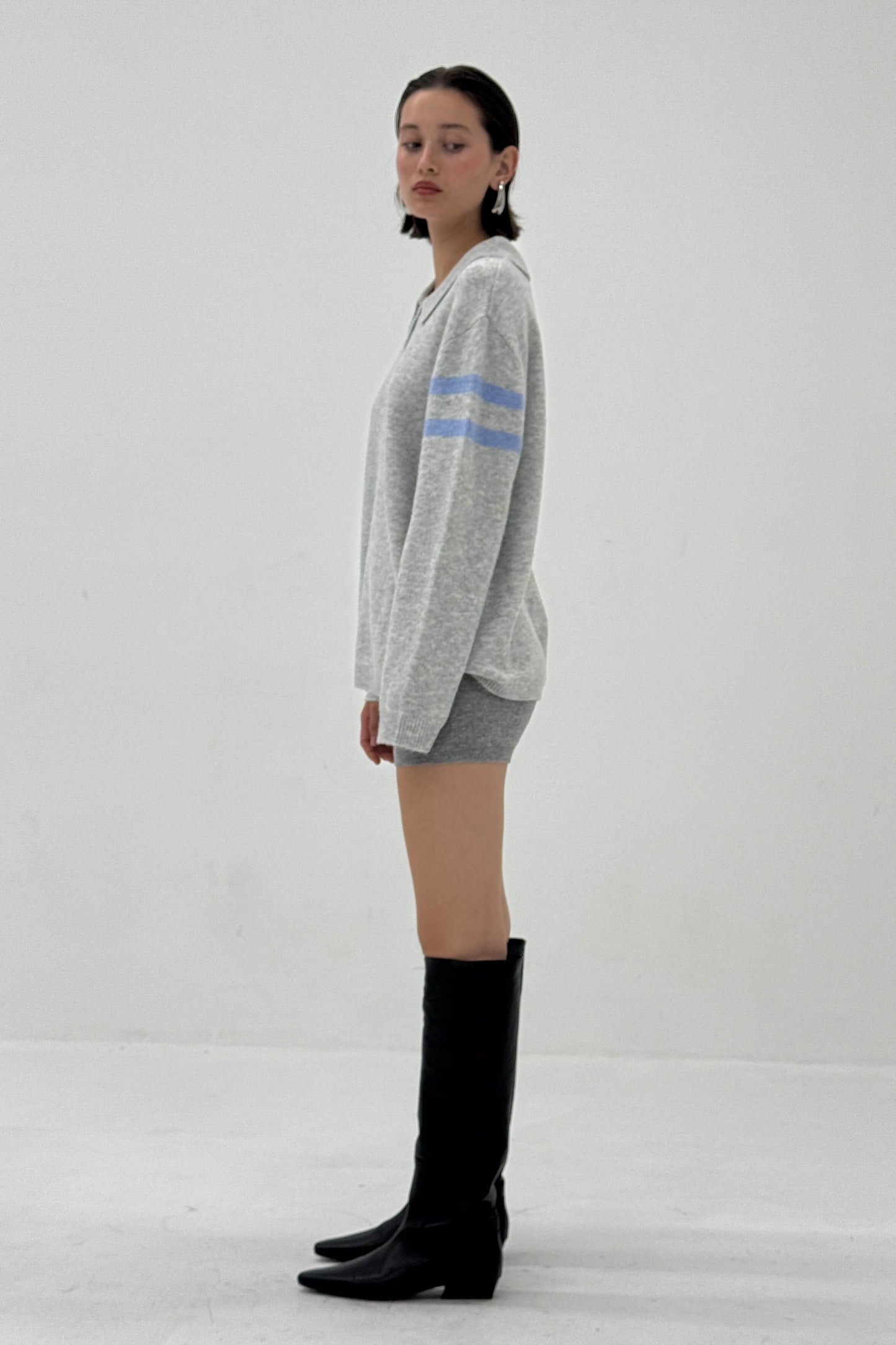 Woman wearing a gray sweater with blue stripes and black knee-high boots on a white background