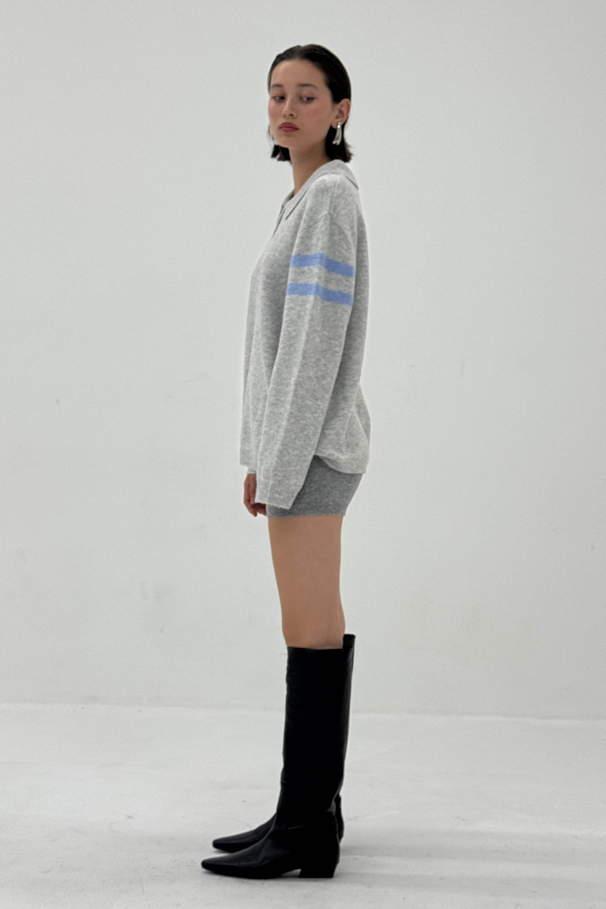 Woman wearing a gray sweater with blue stripes and black knee-high boots on a white background