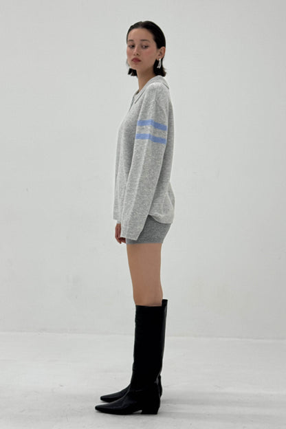 Woman wearing a gray sweater with blue stripes and black knee-high boots on a white background