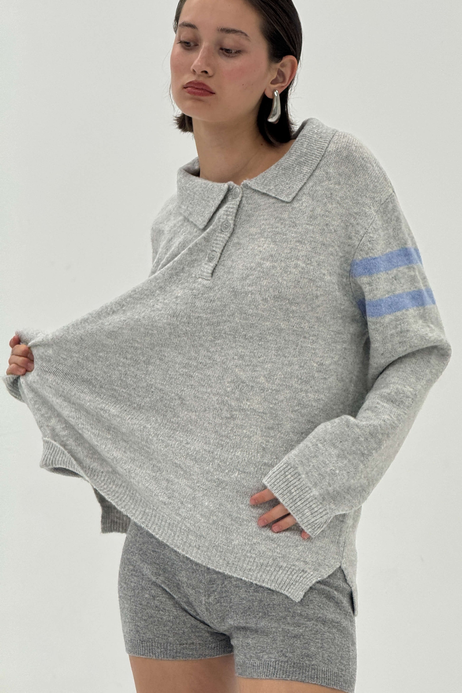 Woman wearing a gray sweater with blue stripes and matching shorts on a white background