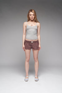 Woman wearing a gray tank top and plaid shorts on a gray background