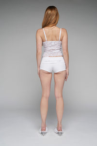 This image features a pair of stylish "cherry micro shorts" in white, showcased on a model who is facing away from the camera. The shorts are characterized by their extreme mini-length and fold-over waistband, which allows for adjustable wear either at a high or low rise.