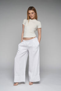 This image features the "Charlotte Pant" in white, showcasing a stylish and comfortable pair of wide-leg linen pants. The model is wearing a size XS and the pants are displayed in a versatile low-rise style, emphasizing their elegant drape and fit.
