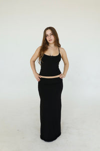 This image features a stylish black maxi skirt, styled in a way that highlights its length and fit. The skirt reaches the floor, providing a full display of its elegant flow and fit.