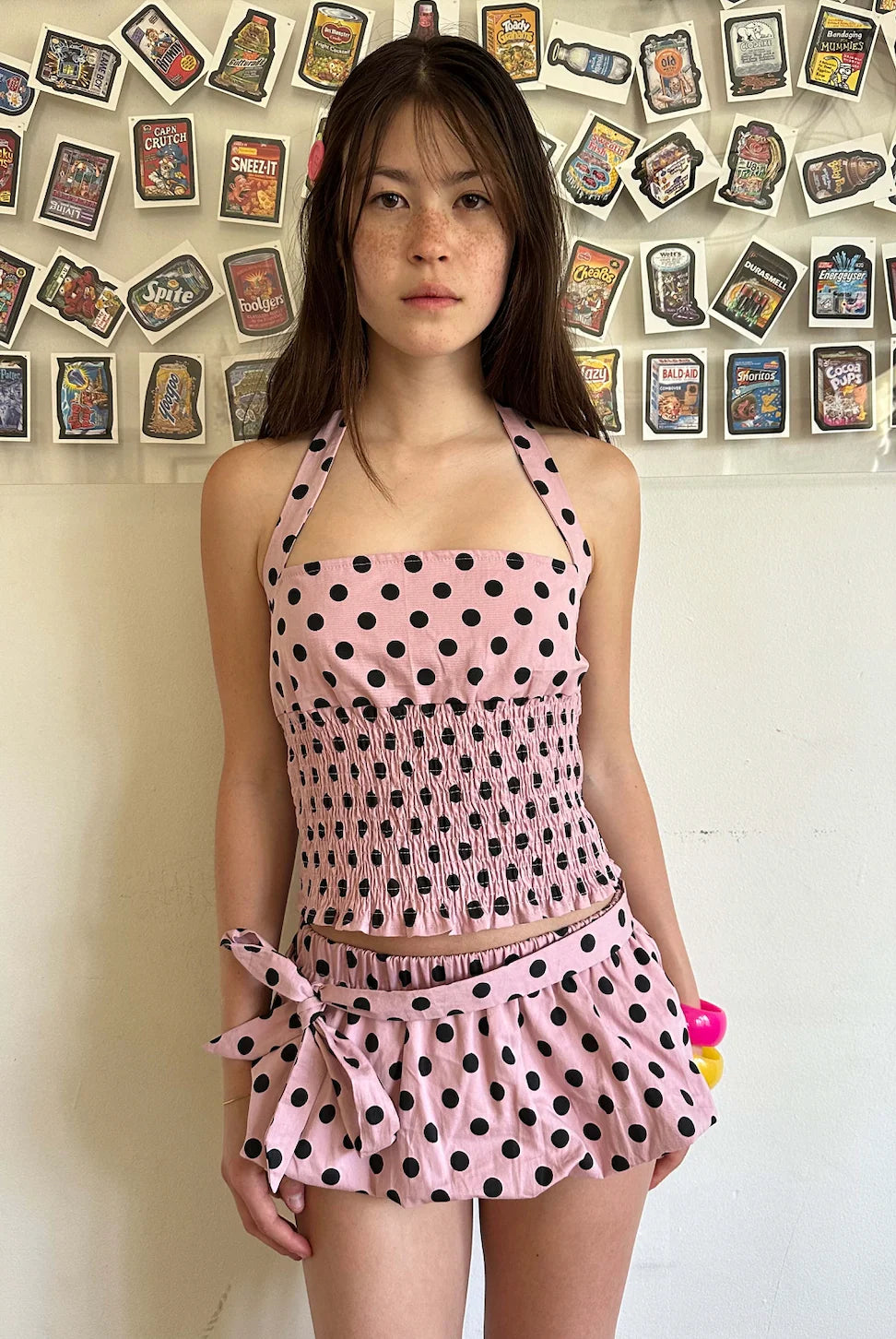 Woman wearing a pink polka dot outfit against a colorful wall.